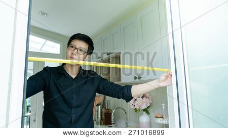 Young Asian Worker Man Using Tape Measure On Door Frame In The Kitchen. Home Interior Designer Measu