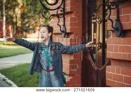 Young Cheerful Child Piddle Near Door Of Building From Red (brown) Brick Near Green Grass Outdoors. 