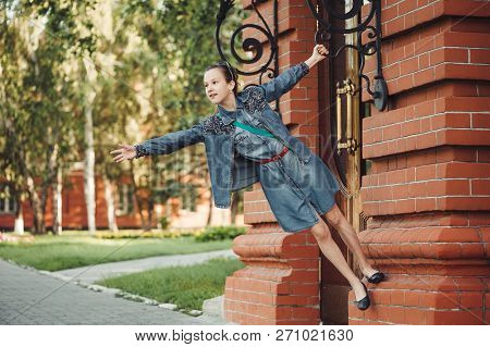 Young Cheerful Child Piddle Near Door Of Building From Red (brown) Brick Near Green Grass Outdoors. 
