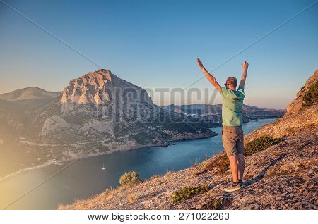 A Young Man Stands On A High Rock And Raised His Hands