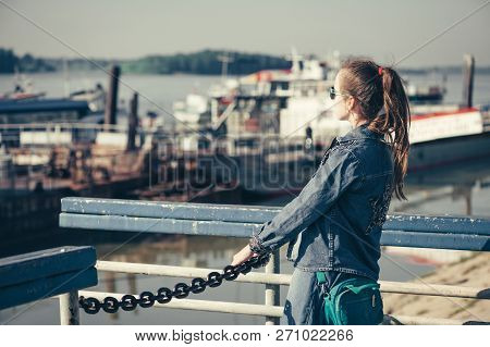 Fun Teenage Girl In Blue Denim Dress Is Walking In River Station. Young Cheerful Child Piddle In Riv