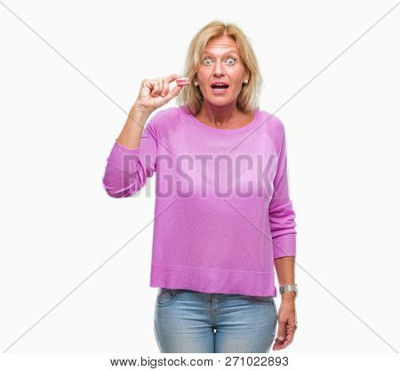 Middle age blonde woman eatin pink macaron biscuit over isolated background scared in shock with a surprise face, afraid and excited with fear expression