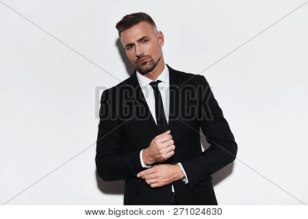 Confident In His Style. Handsome Young Man In Full Suit Adjusting Sleeve And Looking At Camera While