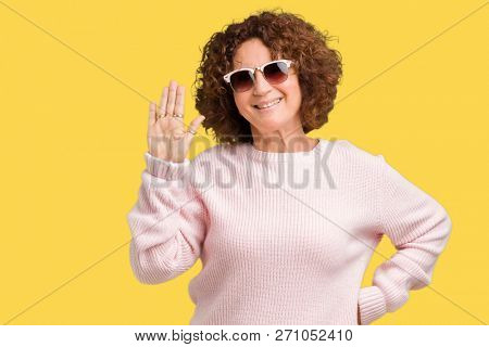Beautiful middle ager senior woman wearing pink sweater and sunglasses over isolated background Waiving saying hello happy and smiling, friendly welcome gesture