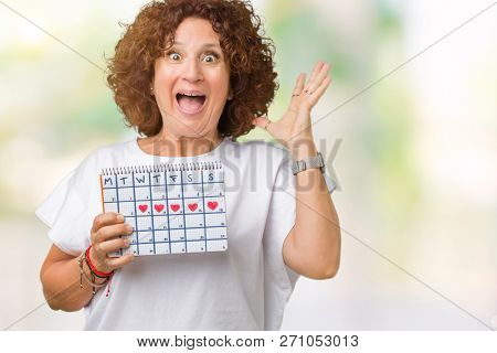 Middle ager senior woman holding menstruation calendar over isolated background very happy and excited, winner expression celebrating victory screaming with big smile and raised hands