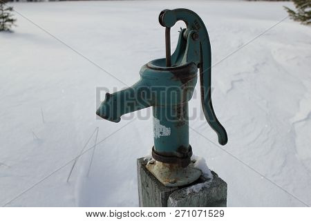 Old, Rusty, Blue Steel Water Pump On A Wooden Post Surrounded By White Snow.