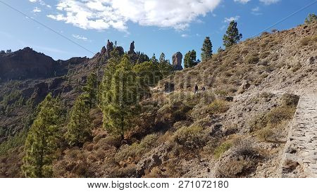 Two Hikers Walking Toward The Roque Nublo In Gran Canaria, Canary Islands.