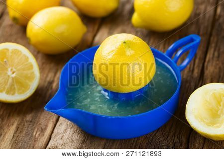 Lemon Half On Blue Lemon Or Citrus Squeezer With Lemons In The Back, Photographed On Wood (selective