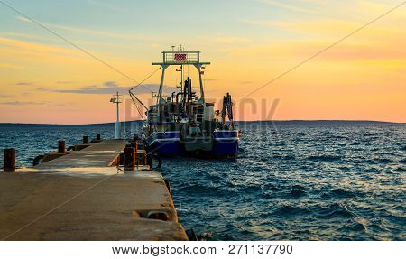 Fishing Boat Moored Or Docked At Pier In Sunset.