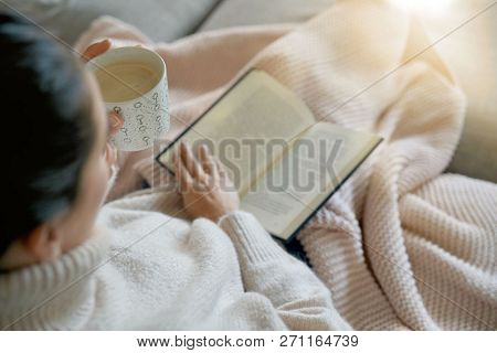 Cosy brunette at home on couch with hot drink and reading