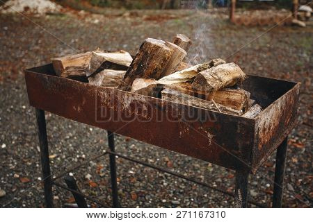 Bonfire In The Grill. Punctured Firewood Lies In A Fire In A Metal Forged Brazier. Fire And Smoke Ar