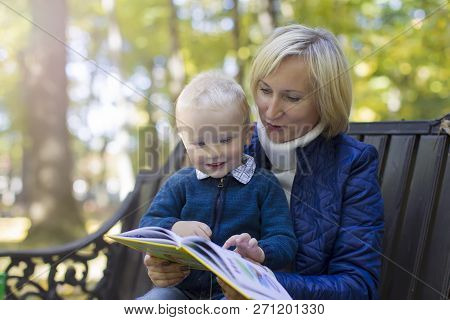 Mom To A Child Reads A Book In The Park For A Walk. Watching A Book With A Child