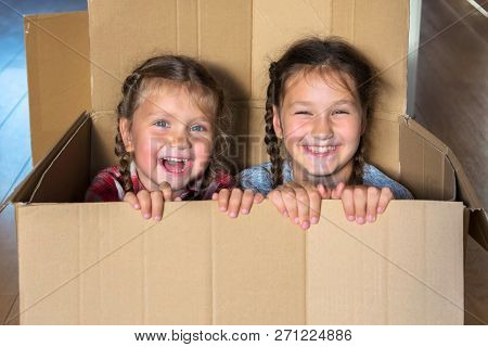 Smiling Children Look Out Of A Large Cardboard Box. Moving To A New Home Concept. Happy Family Reloc