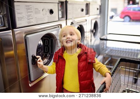 A Little Boy Loads Clothes Into The Washing Machine In Public Laundrette
