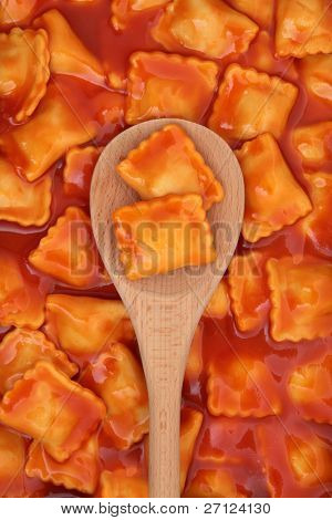 Ravioli pasta in tomato sauce on a wooden spoon and forming a background.