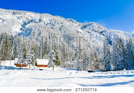 Colorful Wooden Chalets At The Foot Of  The Mountains Surrounding Fusine Lakes In A Sunny Winter Day