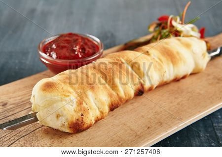 Grilled Khachapuri Made from a Delicious Tender Dough with Melted Burnt Imeretian Cheese Close Up on Rustic Wooden Background with Selective Focus. Traditional Long Bread on a Skewer Fried on Grill