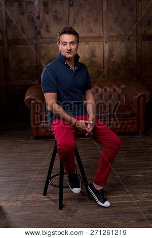 Thoughtful Middle Aged Man In Casual Clothes Sitting On The Bar Stool In The Laconic Room And Lookin