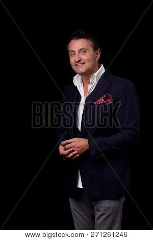 Thoughtful Attractive Man In Elegant Clothes Standing Against The Black Background And Slightly Smil