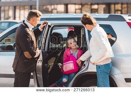 Preteen Daughter Sitting In Car With Opened Door Near Perents