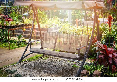 garden bench outdoors / modern swing bench with the roof in the garden flowers spring with green plant background