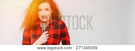 Young Red-haired Girl In A Red Checkered Shirt. A Young Girl Stands With A Microphone