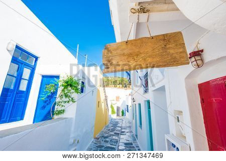 Wooden sign hanging on the rope under the roof. Wide angle of vintage empty signboard in front of narrow Greek street.
