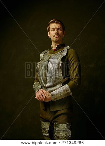 Medieval Knight On Dark Studio Background. Portrait In Low Key Of Brutal Man In Tradishional Retro C