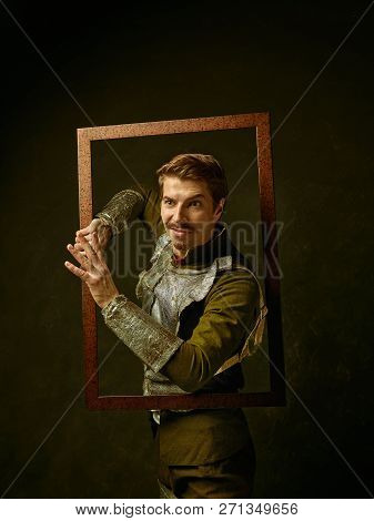 Medieval Knight On Dark Studio Background. Portrait In Low Key Of Brutal Man In Tradishional Retro C