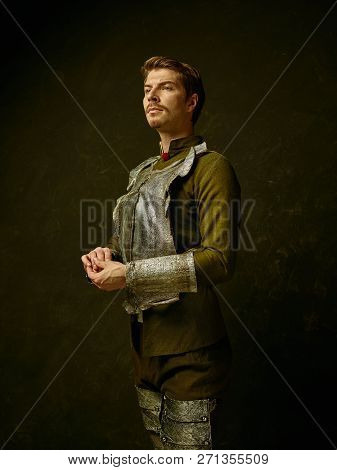 Medieval Knight On Dark Studio Background. Portrait In Low Key Of Brutal Man In Tradishional Retro C