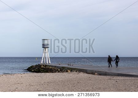 Klampenborg, Denmark - March 25, 2017: A Couple Walking Towards A Lifeguard Tower At Bellevue Beach