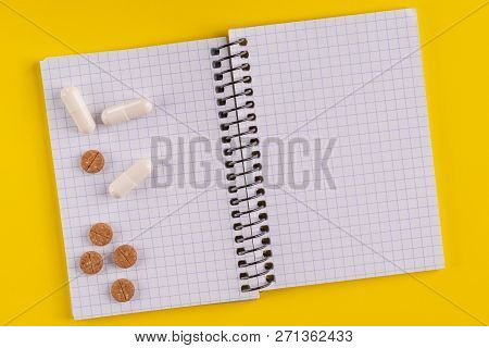 Medical Capsules And Pills Around A Blank Notepad On A Yellow Background, Close-up, Top View, With C