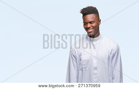 Young arabic african man wearing traditional djellaba over isolated background looking away to side with smile on face, natural expression. Laughing confident.