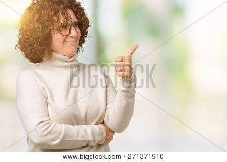 Beautiful middle ager senior woman wearing turtleneck sweater and glasses over isolated background Looking proud, smiling doing thumbs up gesture to the side