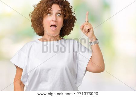 Beautiful middle ager senior woman wearing white t-shirt over isolated background pointing finger up with successful idea. Exited and happy. Number one.