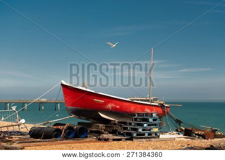 Seagull Flying Over The Red Boat On The Beach With The Peer In The Background. Taken In Kent, Uk.