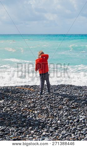 Boy Pulling A Pebble At The Sea From The Beach During A Winter Day