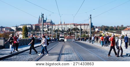 PRAGUE, CZECH REPUBLIC - OCTOBER 14, 2018: Tourists walking by the Manes Bridge over the Vlatva River and the Prague Castle in the background, highlighting the bell towers of the Cathedral