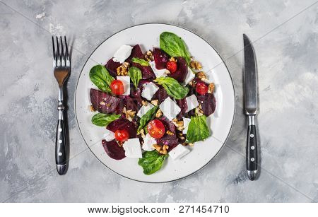 Dish With A Salad Of Feta, Beetroot, Cherry Tomatoes And Walnuts On A Concrete Background. Top View