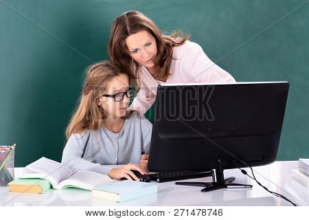 Teacher Teaching Her Student On Computer With Books On Desk In Classroom