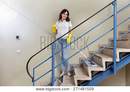 Young Female Janitor Cleaning Staircase With Mop