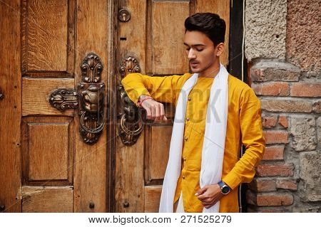 Indian Stylish Man In Yellow Traditional Clothes With White Scarf Posed Outdoor Against Old Gates.