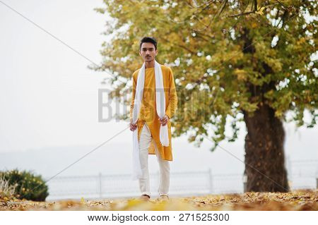 Indian Stylish Man In Yellow Traditional Clothes With White Scarf Posed Outdoor Against Autumn Leave