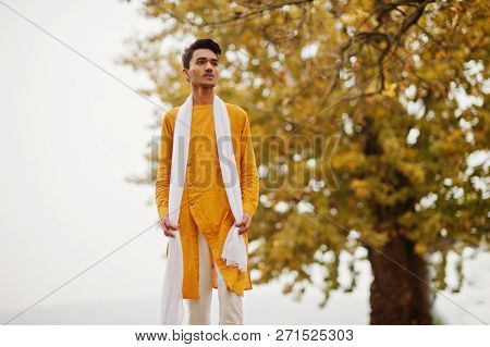 Indian Stylish Man In Yellow Traditional Clothes With White Scarf Posed Outdoor Against Autumn Leave