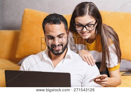 Pretty Long-haired Girl In Pullover Wearing Glasses Holding Credit Card And Sitting On The Yellow So
