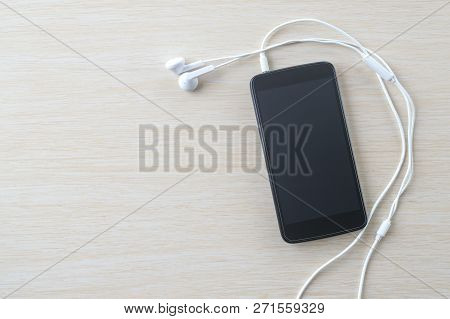 Black Smartphone With White Headphones On A Beige Board.