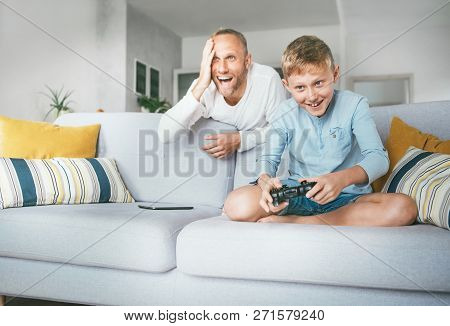 Father Watching His Son Playing Tv Video Game Using The Gamepad And Emotionaly Reacts. Liitle Kids A