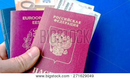 Hands Holding Passports On Blue Background. Citizenship Of Estonia And Russia. Citizenship Of Europe