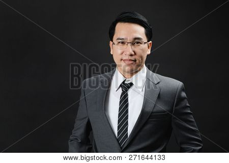 Portrait Of Asian Business Man In Suit And Tie, Looks Confidence And Trustworthy. Isolated In Black 