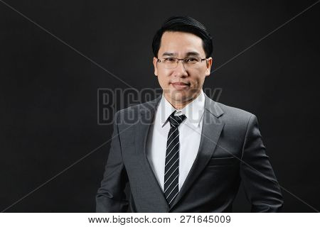 Portrait Of Asian Business Man In Suit And Tie, Looks Confidence And Trustworthy. Isolated In Black 